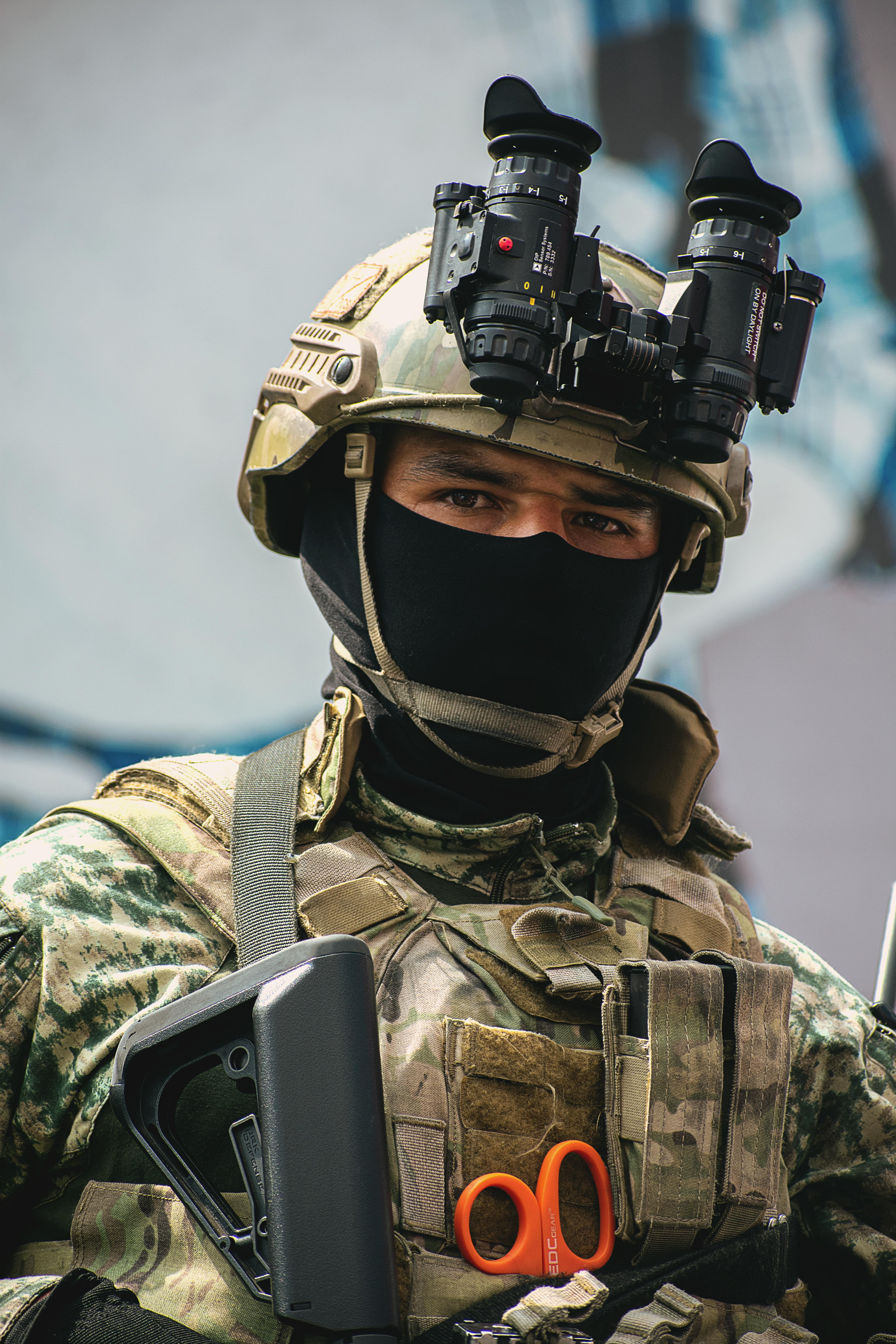 A young soldier wearing a helmet and a cap with camouflage, along with a vest, with only his eyes visible.
