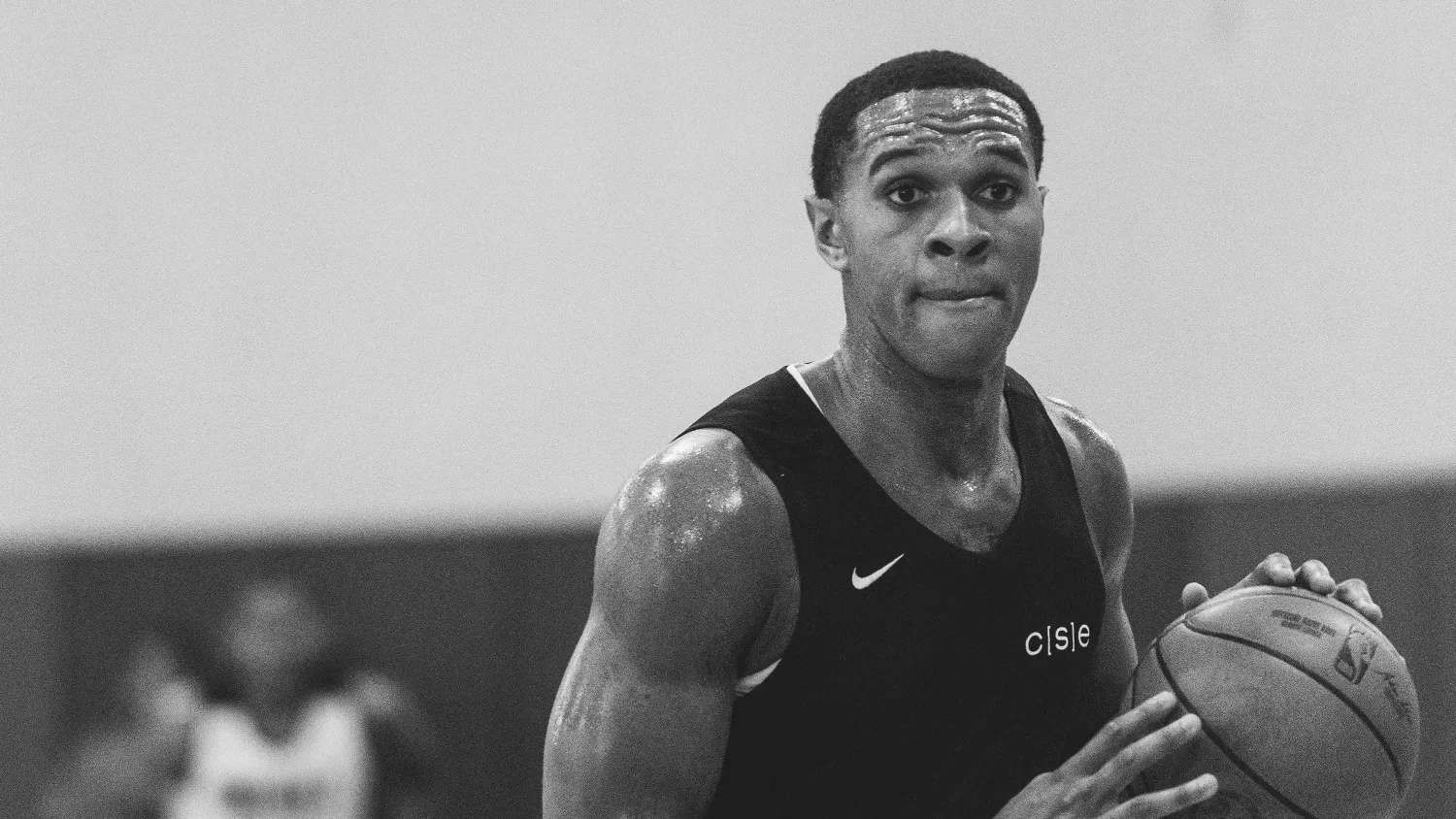 A basketball player in a black CISE outfit dribbles a basketball on an indoor court, with retired jerseys hanging in the background and the CISE Athletes logo at the bottom.
