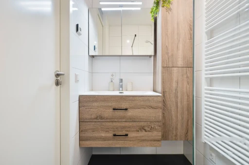 Het houten wastafelmeubel met spiegelkast en een hoge opbergkast in de badkamer.
