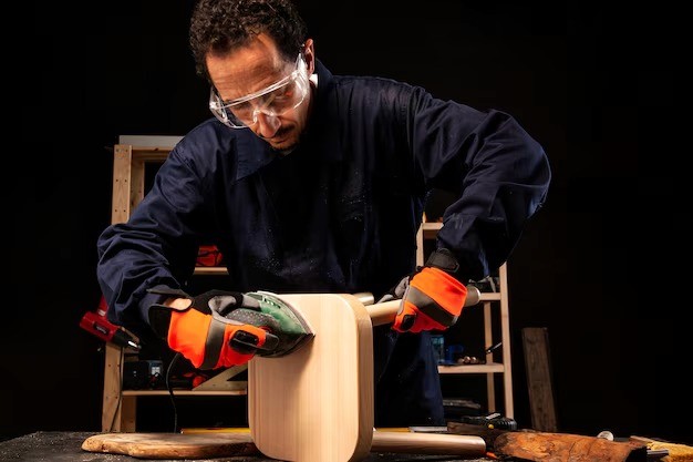 Man assembling a white table with brown legs. The man is wearing a blue jumpsuit and leaning over the furniture.