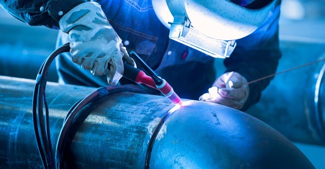 Zertifizierter Facharbeiter bei der Ausführung einer präzisen WIG-Schweißnaht an einem industriellen Rohrleitungssystem für den Anlagenbau