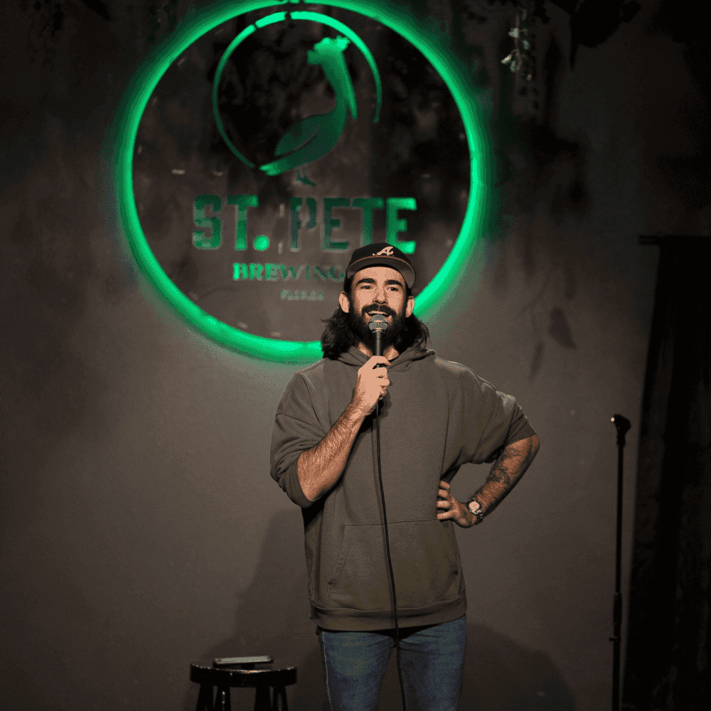 A male comedian with his hand on his hip on stage at a St Pete Standup show