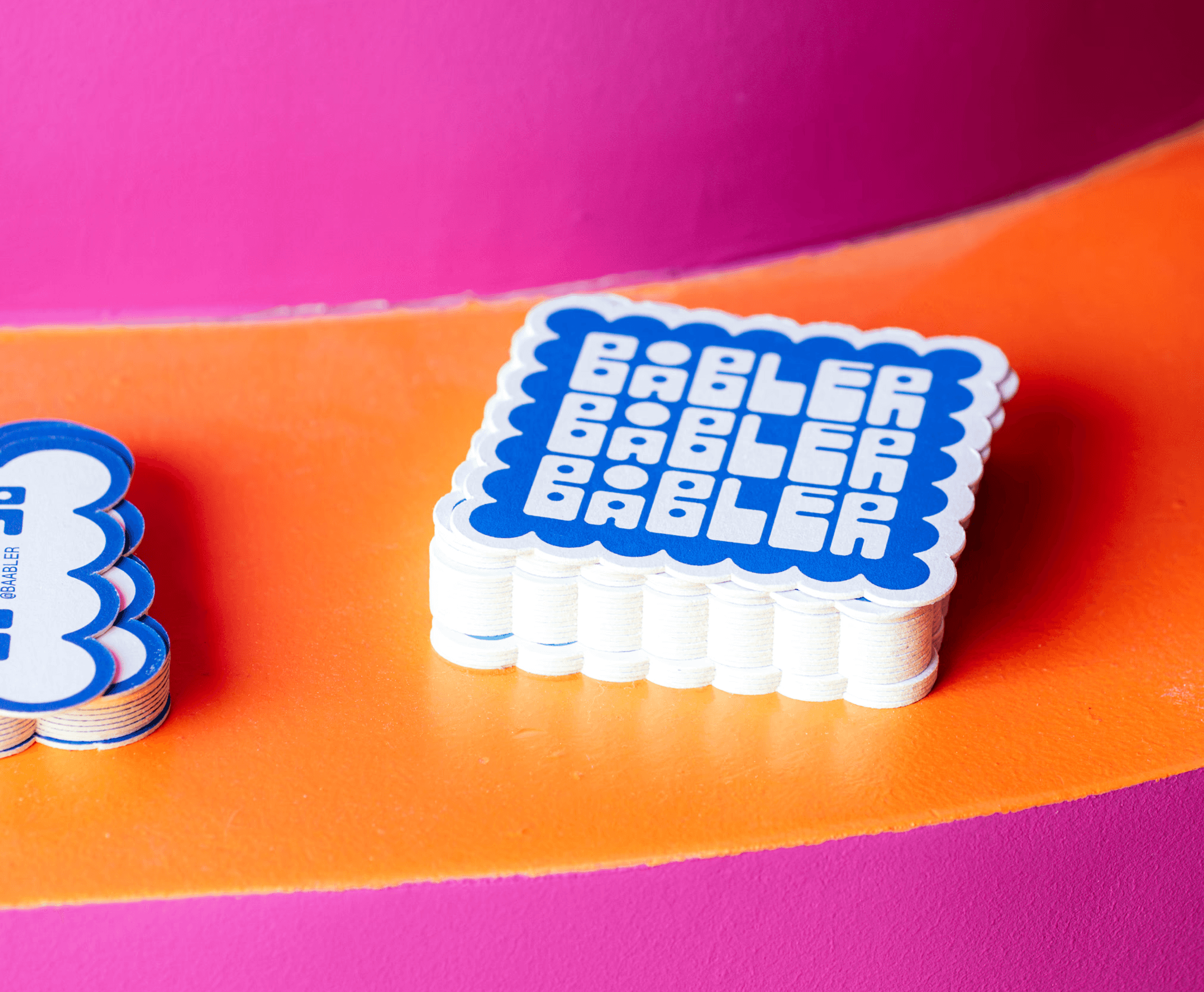 Coaster designs for Båbler wine bar laying in a stack on a orange and pink table.