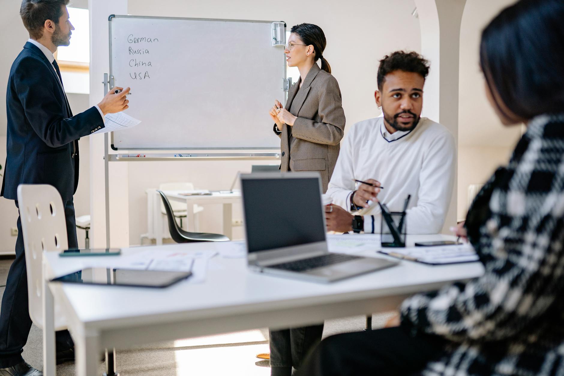 A group of diverse students in professional attire presenting a business plan using a flip chart in a boardroom.