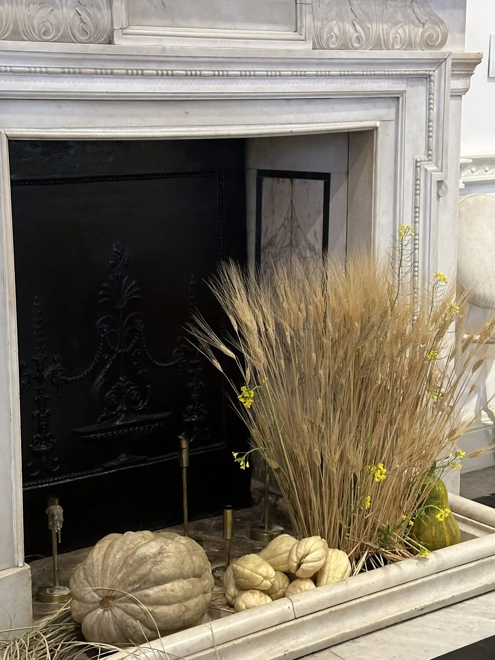 Decoración de chimenea con espigas secas y calabazas naturales para ambientación otoñal elegante.