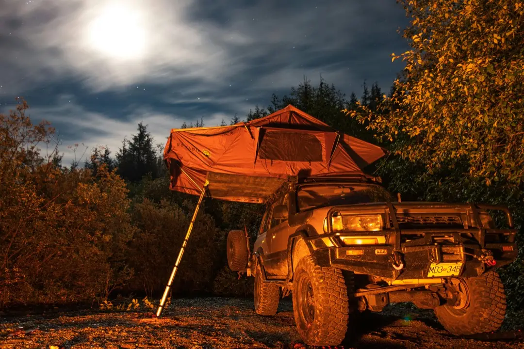 A rugged four wheel drive vehicle parked with the rooftop tent set up for the night