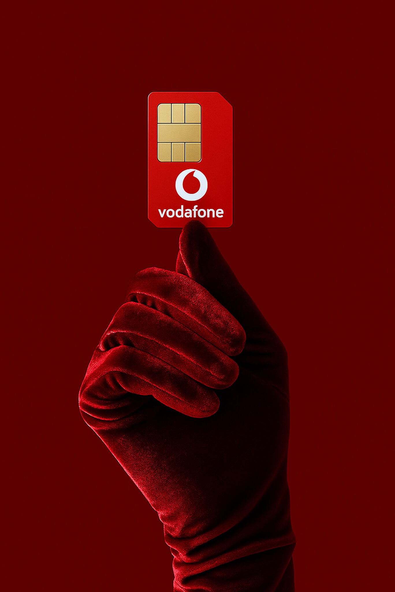 A red velvet-gloved hand holding a Vodafone SIM card against a deep red background.