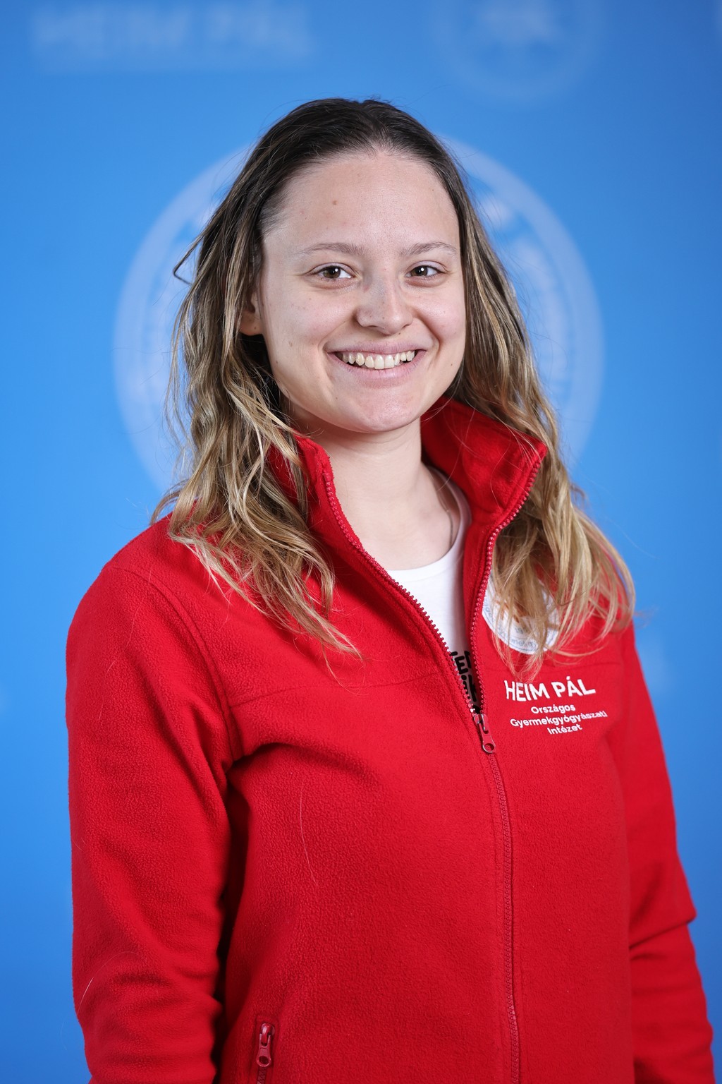 Hosszúhajú szőke mosolygós nő piros kardigánban