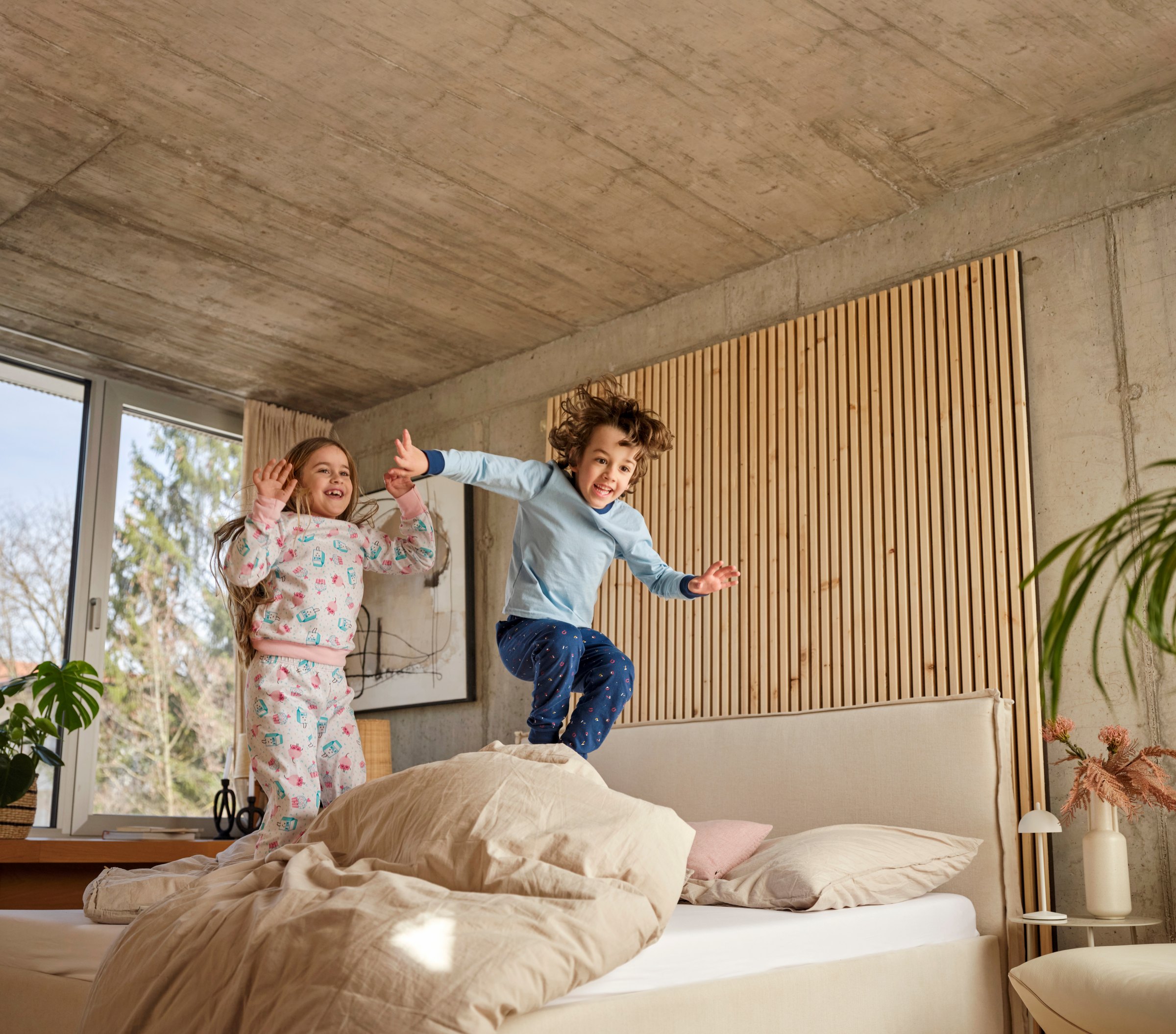Zwei Kinder springen im Schlafzimmer auf das Bett