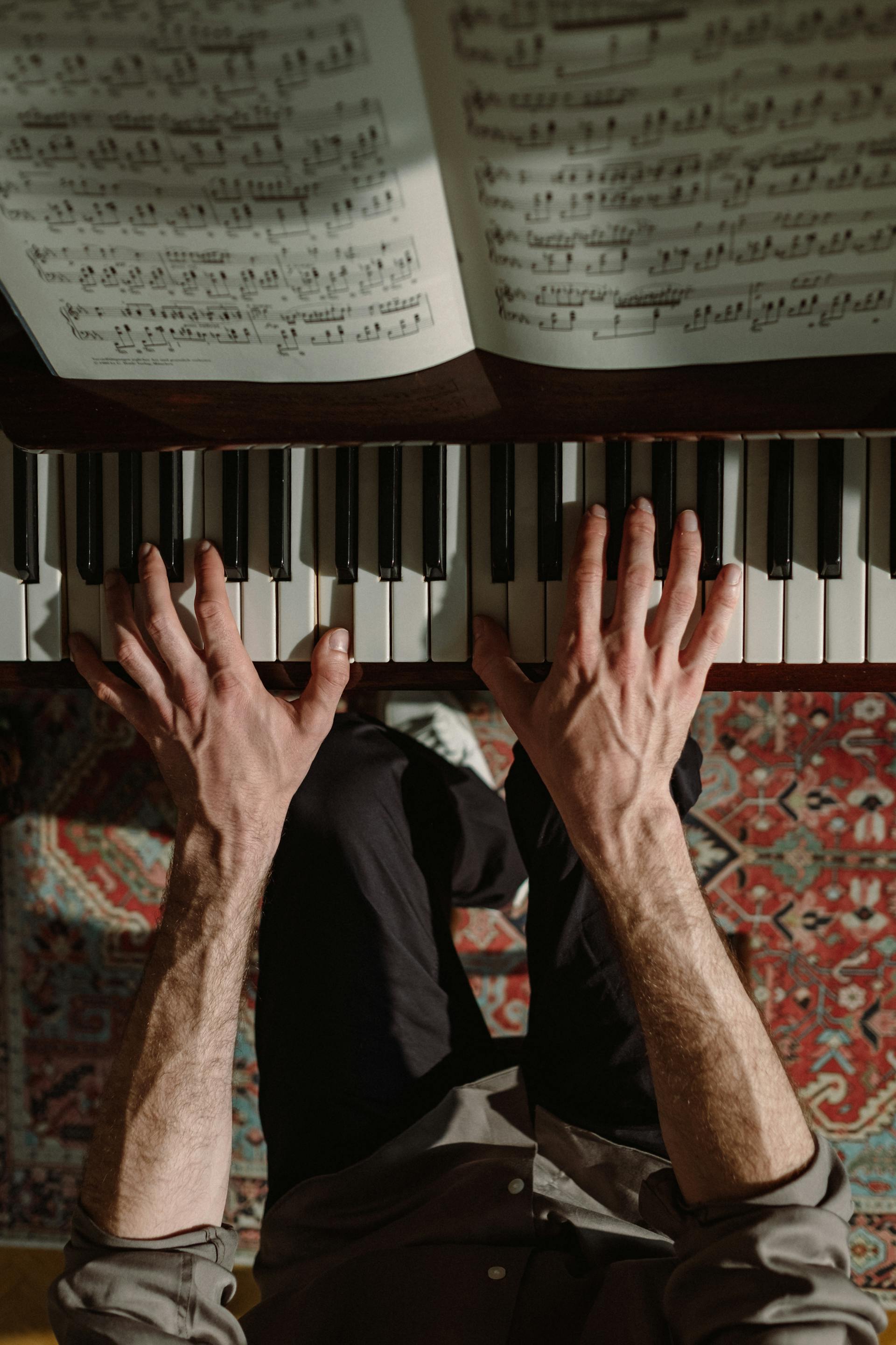 An overhead view showing a person's hands playing chords on a piano keyboard with open sheet music above.