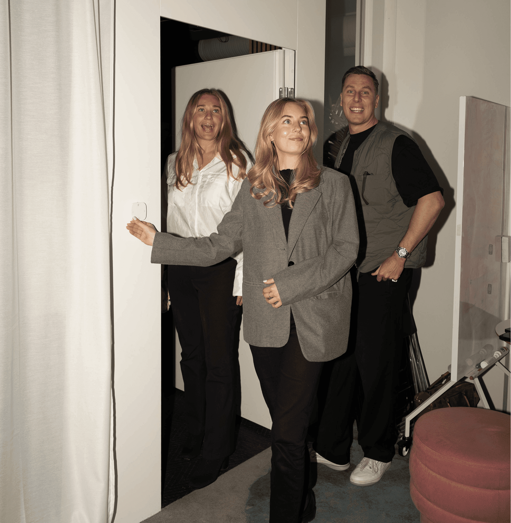 Three people entering a room together, smiling and looking ahead, captured indoors in a casual setting.