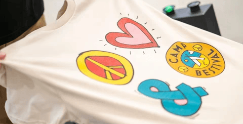 Smiling man in a white hoodie and black pants standing confidently on a bright green football field with empty stadium seats behind.