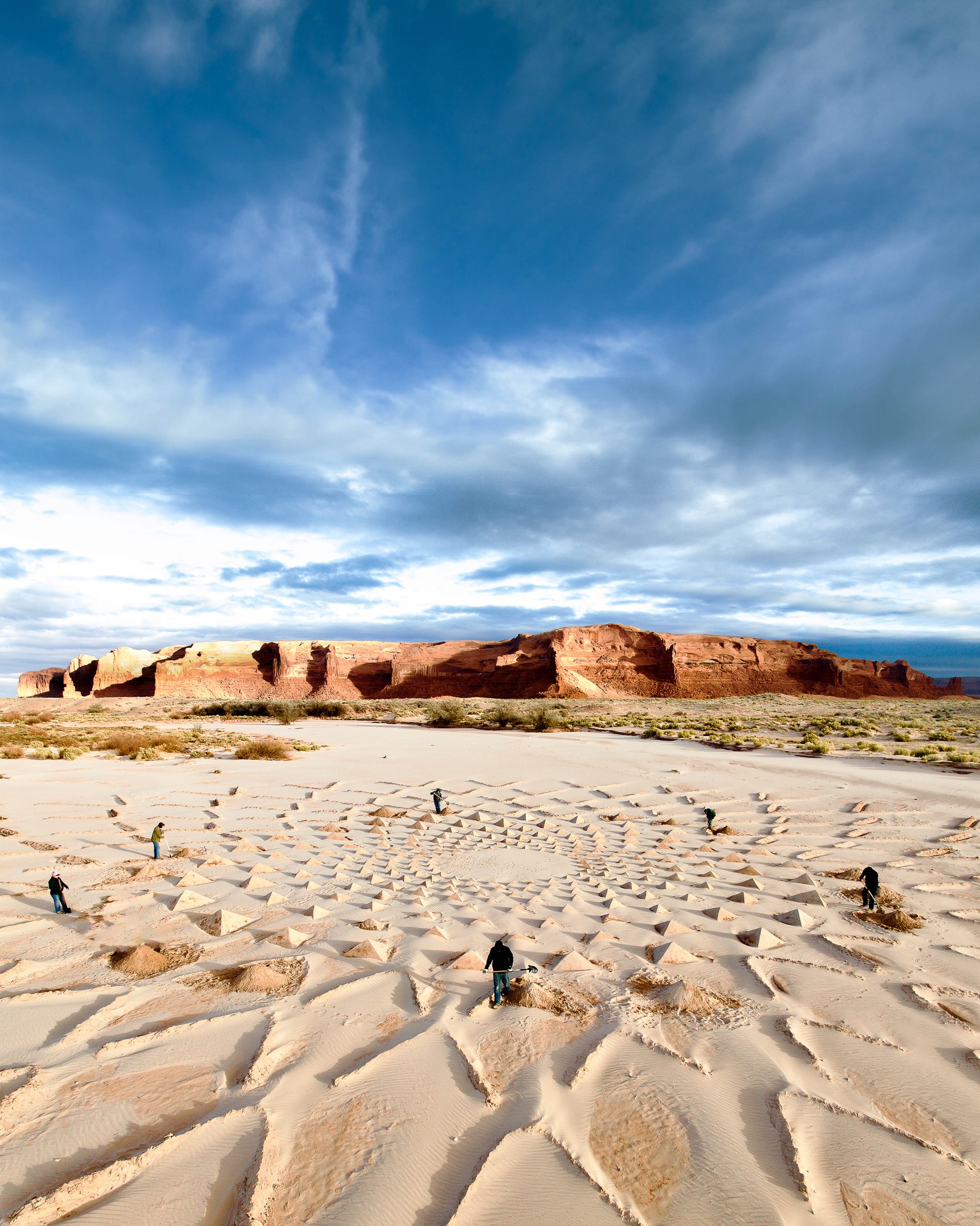 A group of people digging in the sand to build a massive piece of land art in a riverbed in front of Arizona red rocks