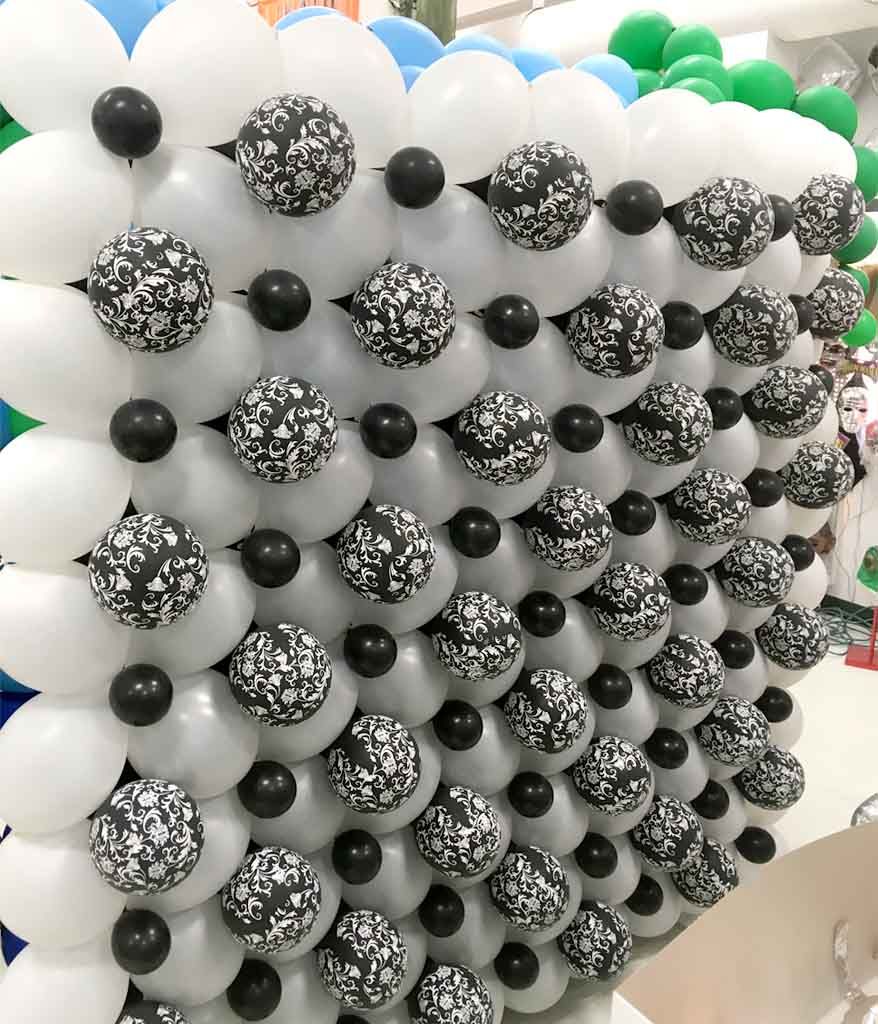 A decorative wall of balloons features a grid pattern with alternating black and white balloons, some adorned with intricate floral designs, creating an eye-catching display ideal for parties or events.