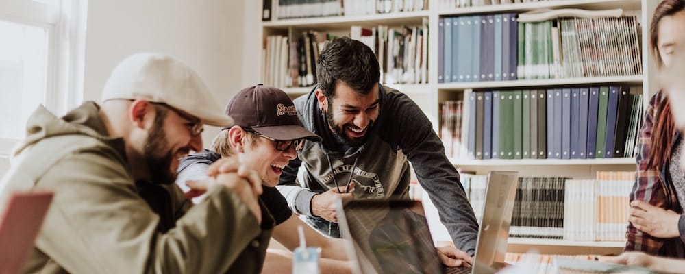 Team collaboration in a library with smiling people around a laptop.