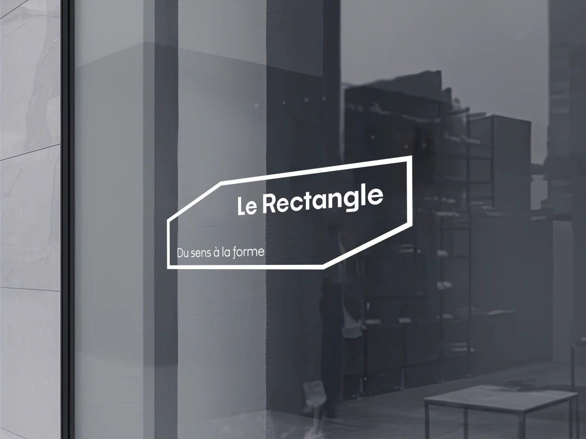 Logo Le Rectangle appliqué en vitrophanie blanche sur la vitrine sombre des locaux de l'agence.
