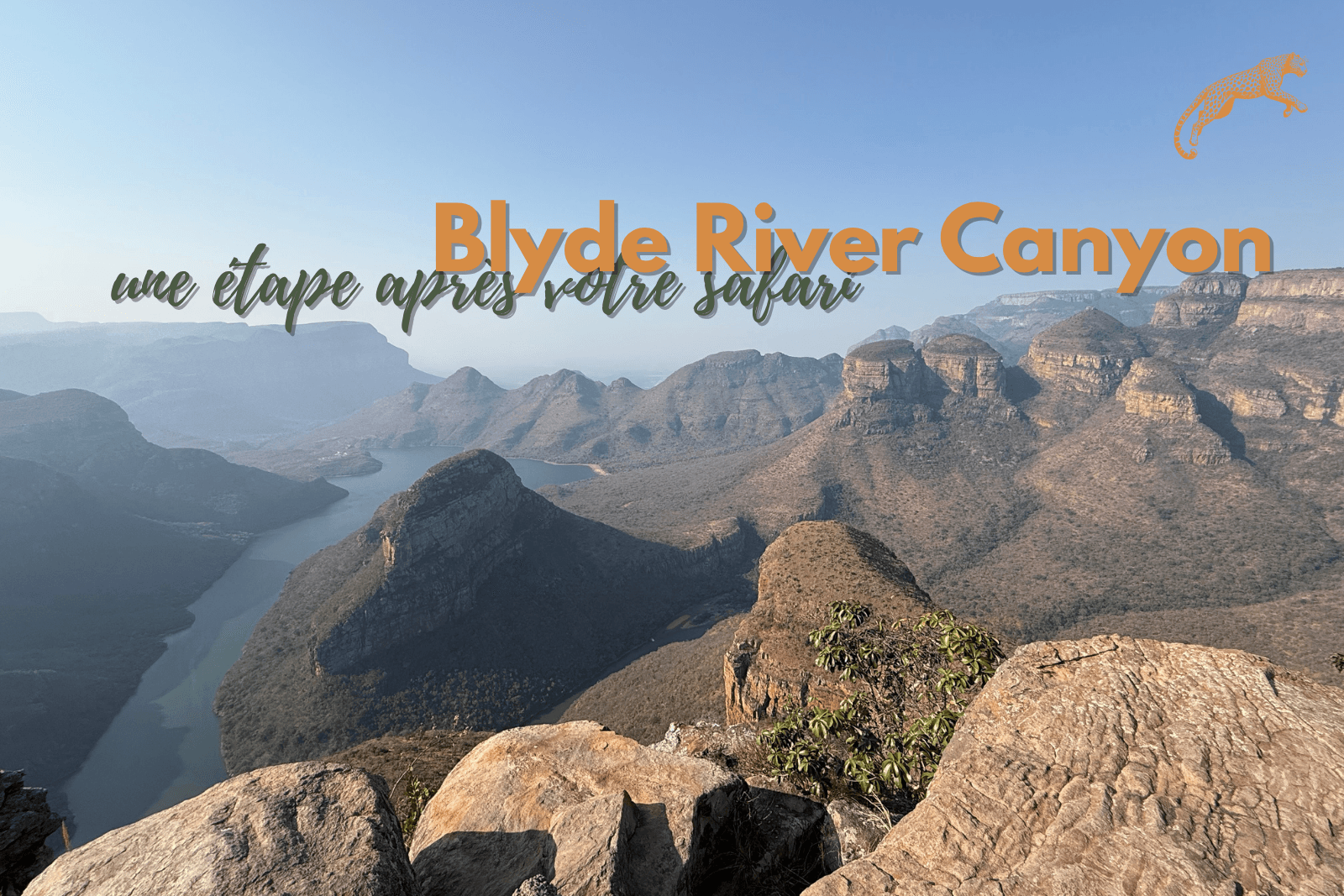 Paysage du Blyde River Canyon avec falaises abruptes, rivière en contrebas et végétation verte sous un ciel bleu dégagé.