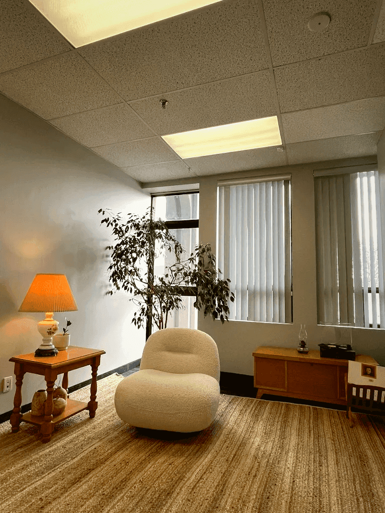 Cozy office corner with armchair, lamp, and plant.