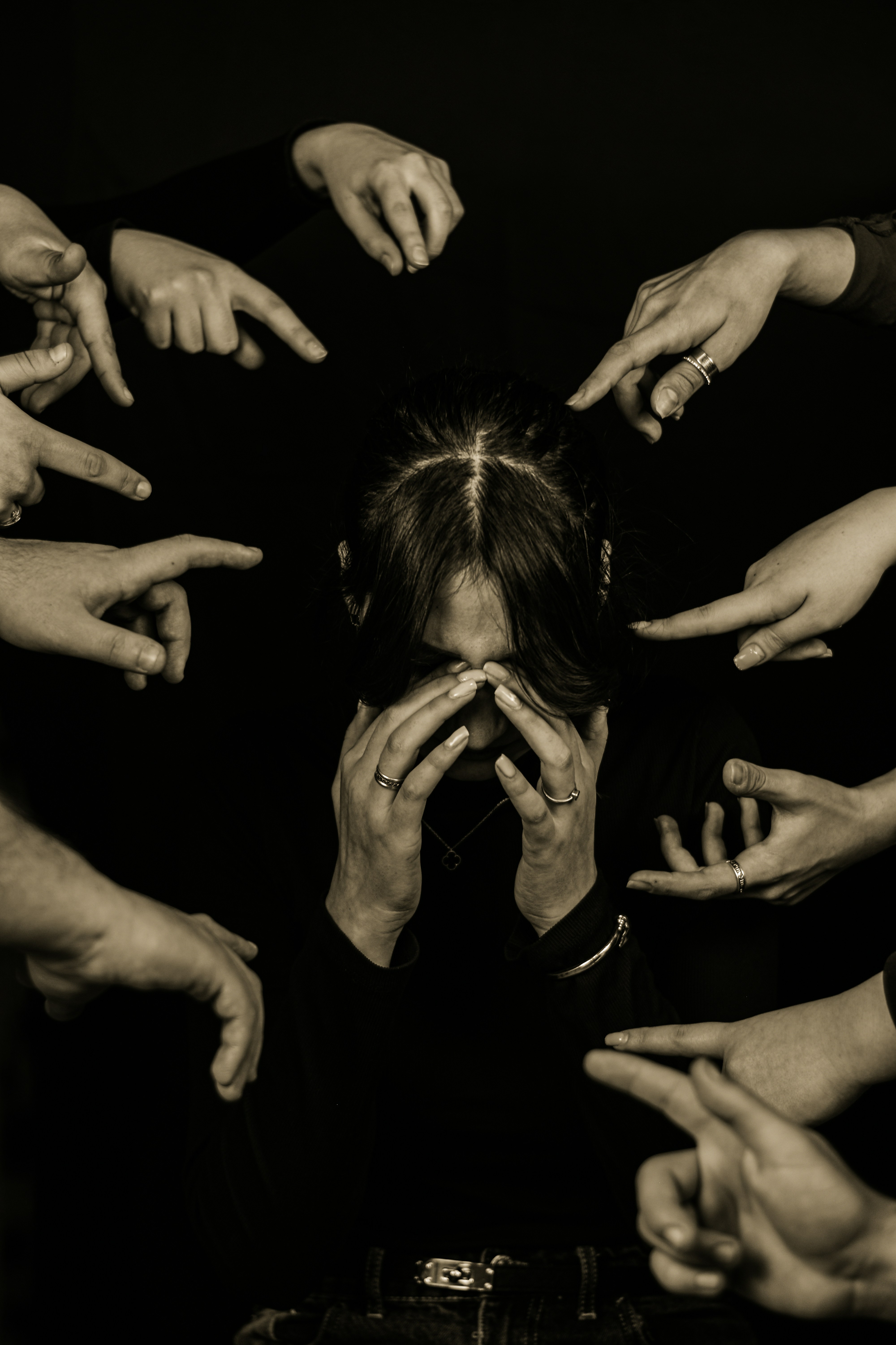 Person surrounded by pointing fingers in dark setting