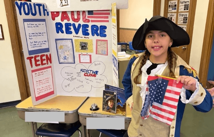 A student dressed as Paul Revere beside her biography project board
