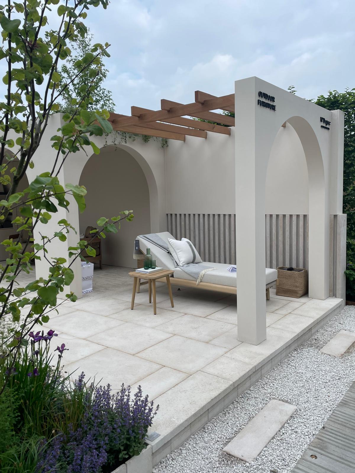 A stylish patio with a lounge chair, surrounded by greenery and architectural elements under a cloudy sky.