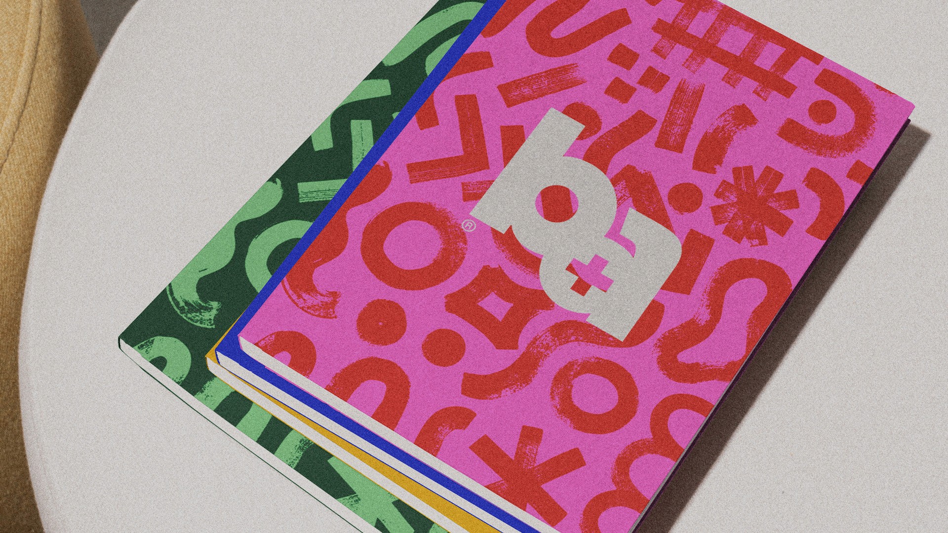 Four colorful notebooks with a fun scribbled pattern and the brand aid logo on topp stacked on a chair.