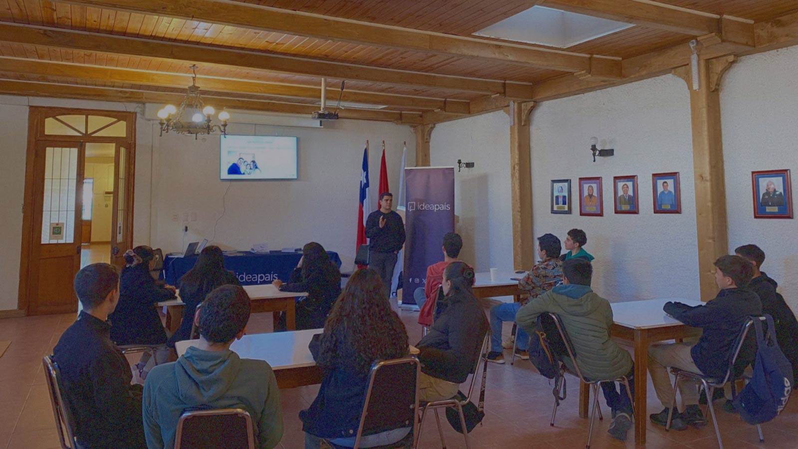 Portada de Colectivos de formación escolares, programa de formación de IdeaPaís, mostrando a escolares que escuchan a un expositor, sentados en grupos de tres o cuatro personas alrededor de mesas. 