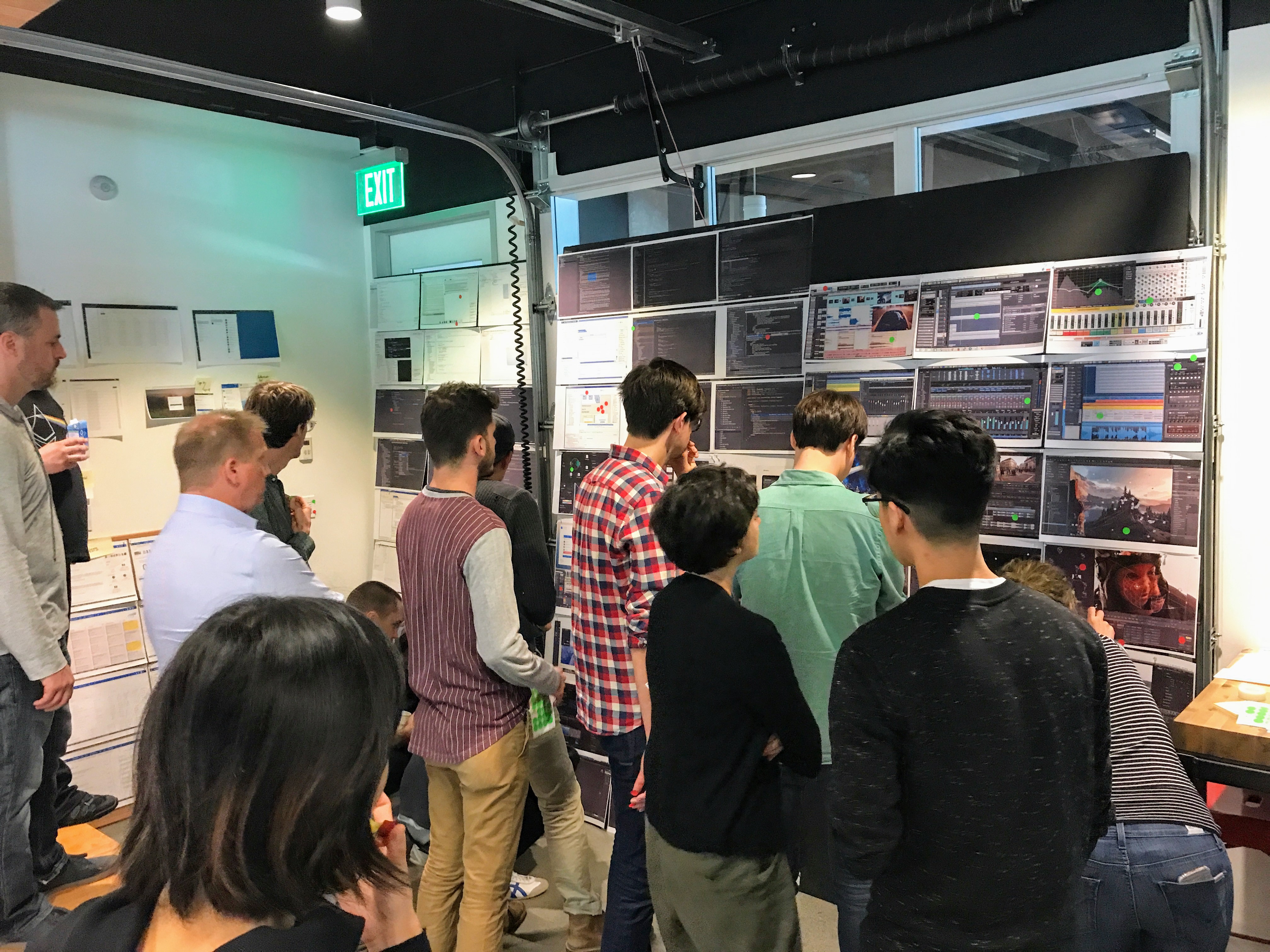 Group of designers gathered around a wall displaying various software interfaces and data visualizations.