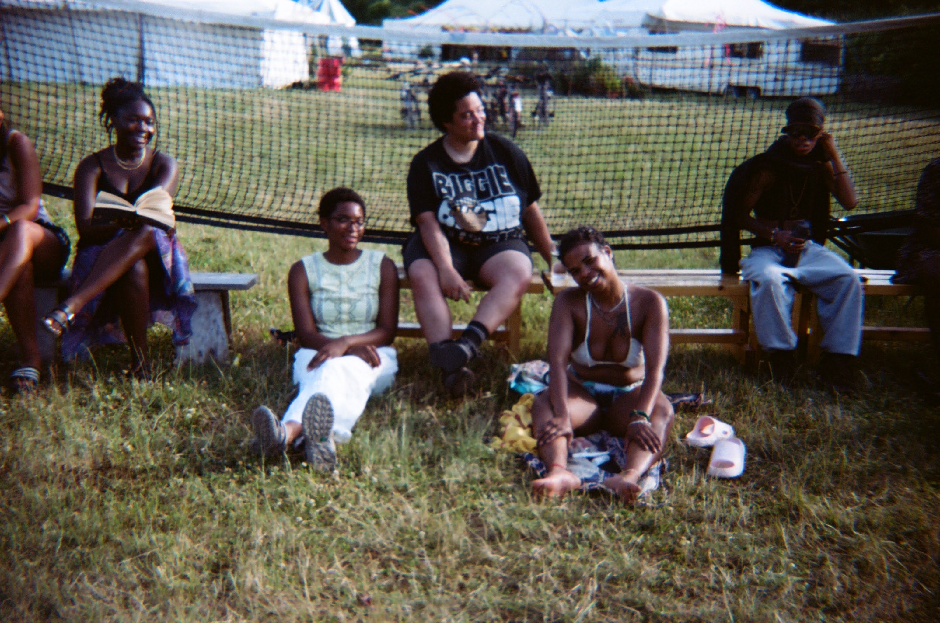 A group of people sit down on a bench and on the grass, smiling and chatting
