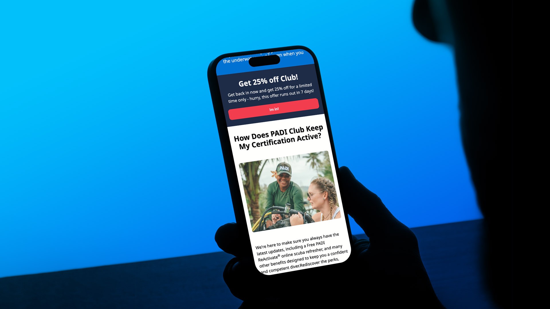 Silhouetted person holding a smartphone displaying a PADI Club reactivation email campaign featuring promotional messaging, membership benefits, and mobile-first email content against a blue-lit background.