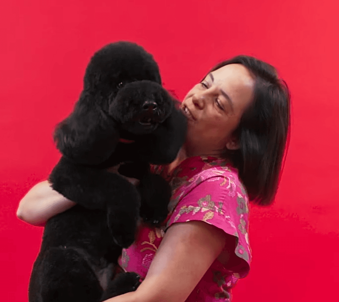 Happy woman hugging her small black dog against a pink background to express love and joyful grooming connection.