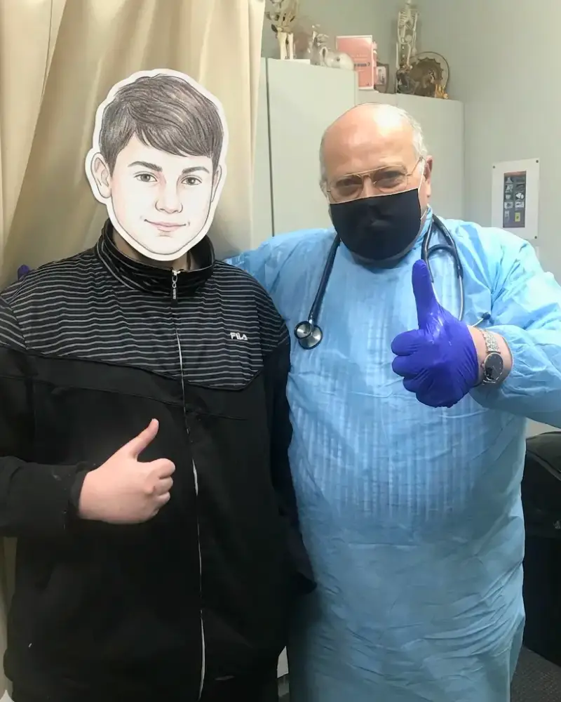 Dr Ashraf Saddik giving a thumbs-up alongside a teenage patient in a black jacket inside a consultation room in Coburg, serving Melbourne's northern suburbs.