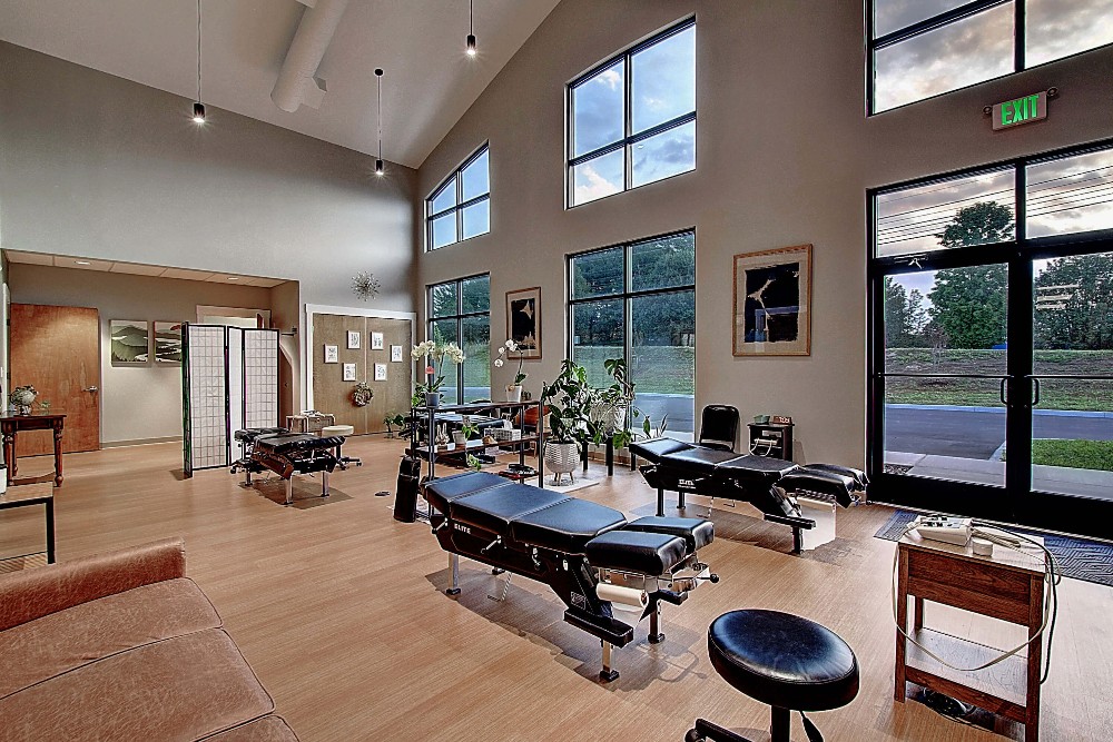 Modern interior with large windows, wooden floors, a table, and various furniture, creating a spacious ambiance.