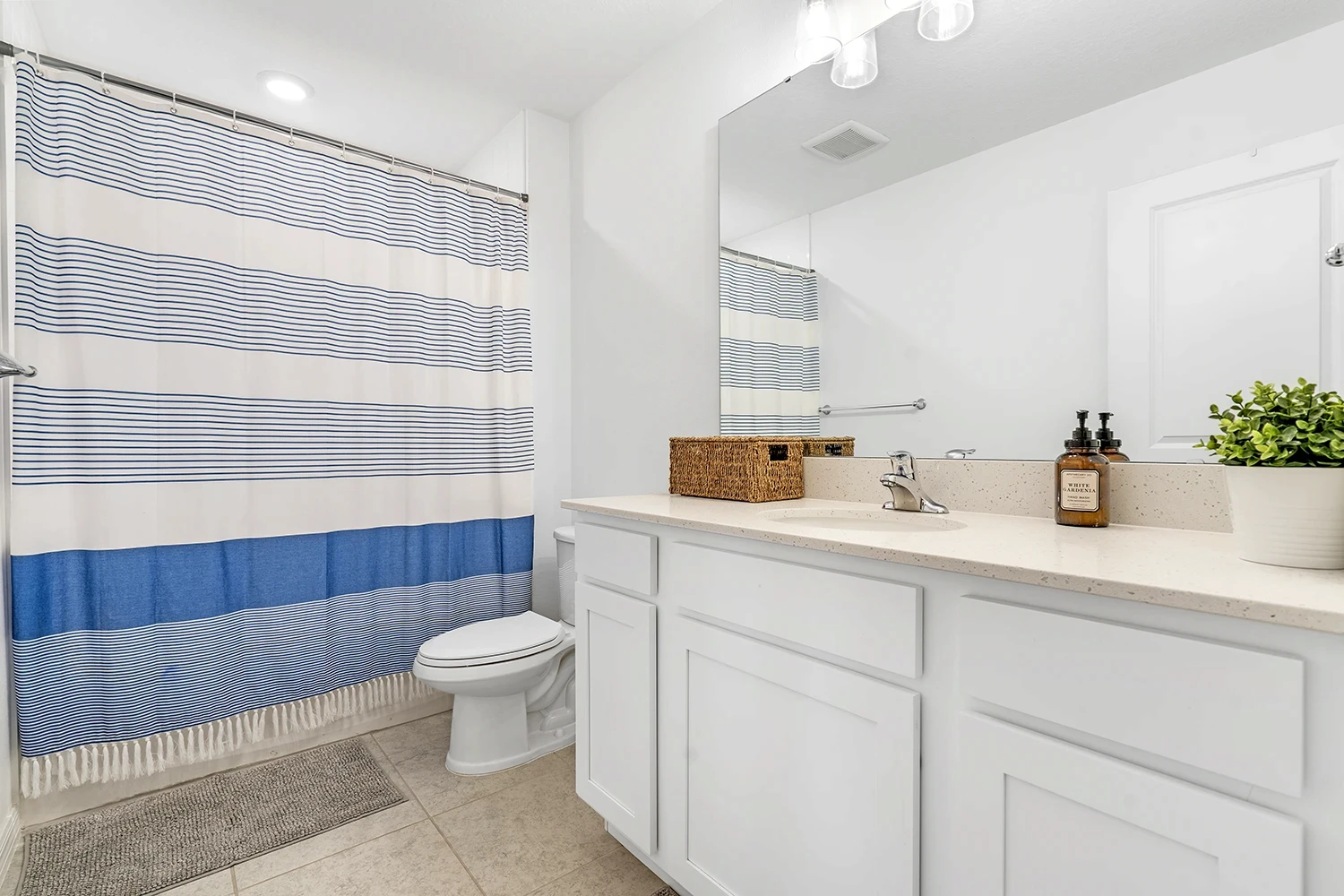 Bathroom with a white vanity, large mirror, blue-and-white striped shower curtain and light neutral tile, in a Polk County townhome