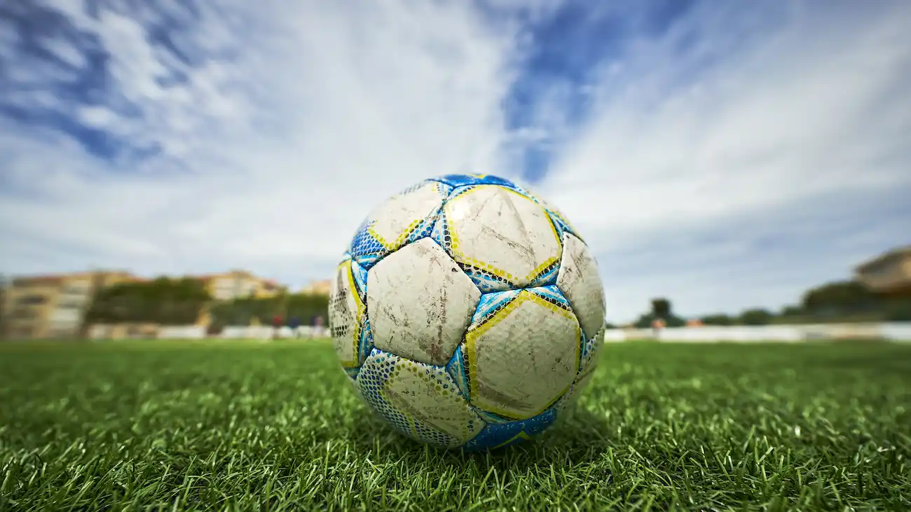 This image features a close-up of a seasoned football resting on the artificial green turf, poised for the next play. The worn textures of the ball, marked from rigorous matches, contrast beautifully with the immaculate, synthetic blades of grass that replicate a professional pitch. Above, the sky opens in a breath-taking display of azure, with soft clouds creating a serene backdrop. The image is rich in detail, offering a tangible sense of the sport's vibrancy and the passion it inspires.This image features a close-up of a seasoned football resting on the artificial green turf, poised for the next play. The worn textures of the ball, marked from rigorous matches, contrast beautifully with the immaculate, synthetic blades of grass that replicate a professional pitch. Above, the sky opens in a breath-taking display of azure, with soft clouds creating a serene backdrop. The image is rich in detail, offering a tangible sense of the sport's vibrancy and the passion it inspires.