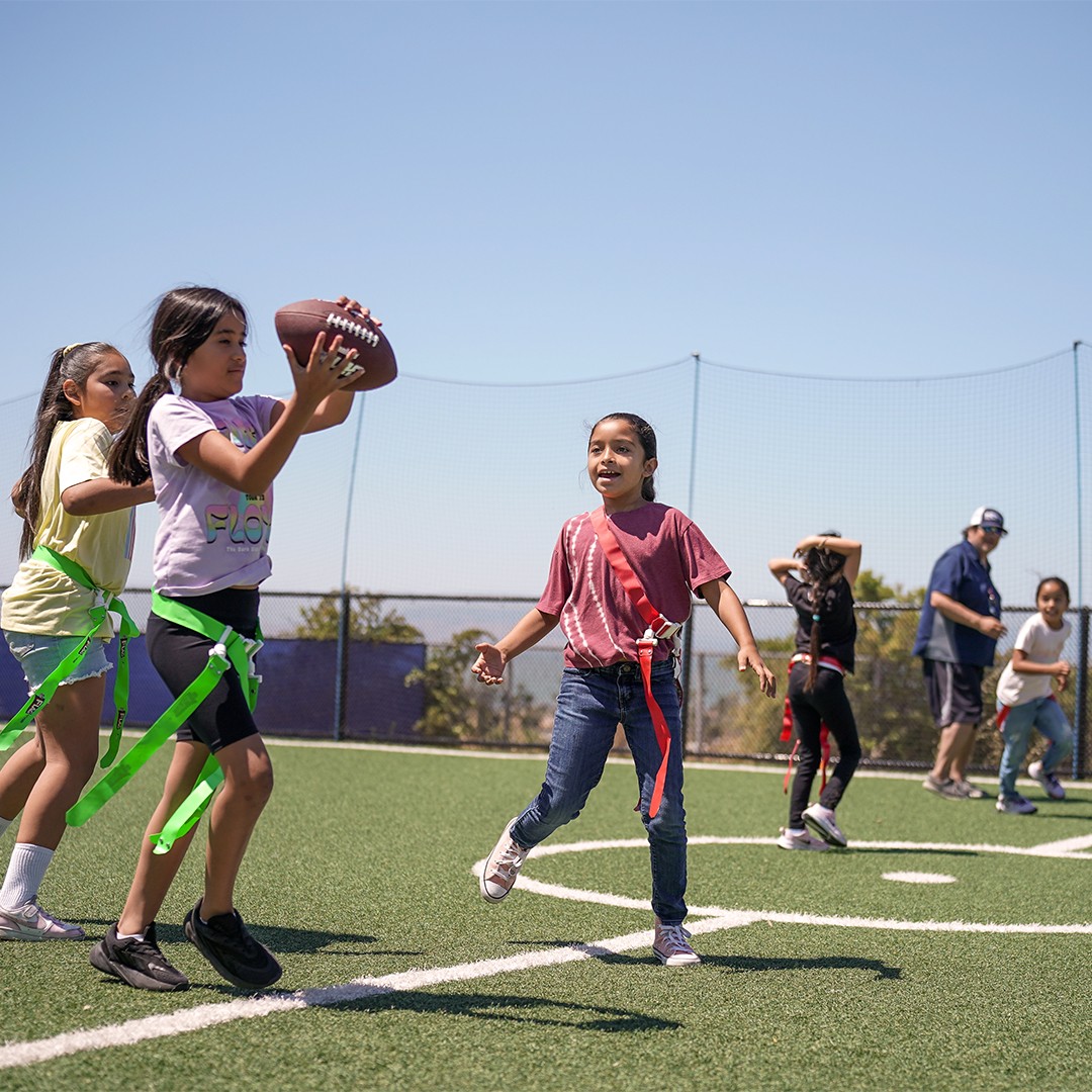 girls playing flag football during an outdoor after-school sports program on a school field
