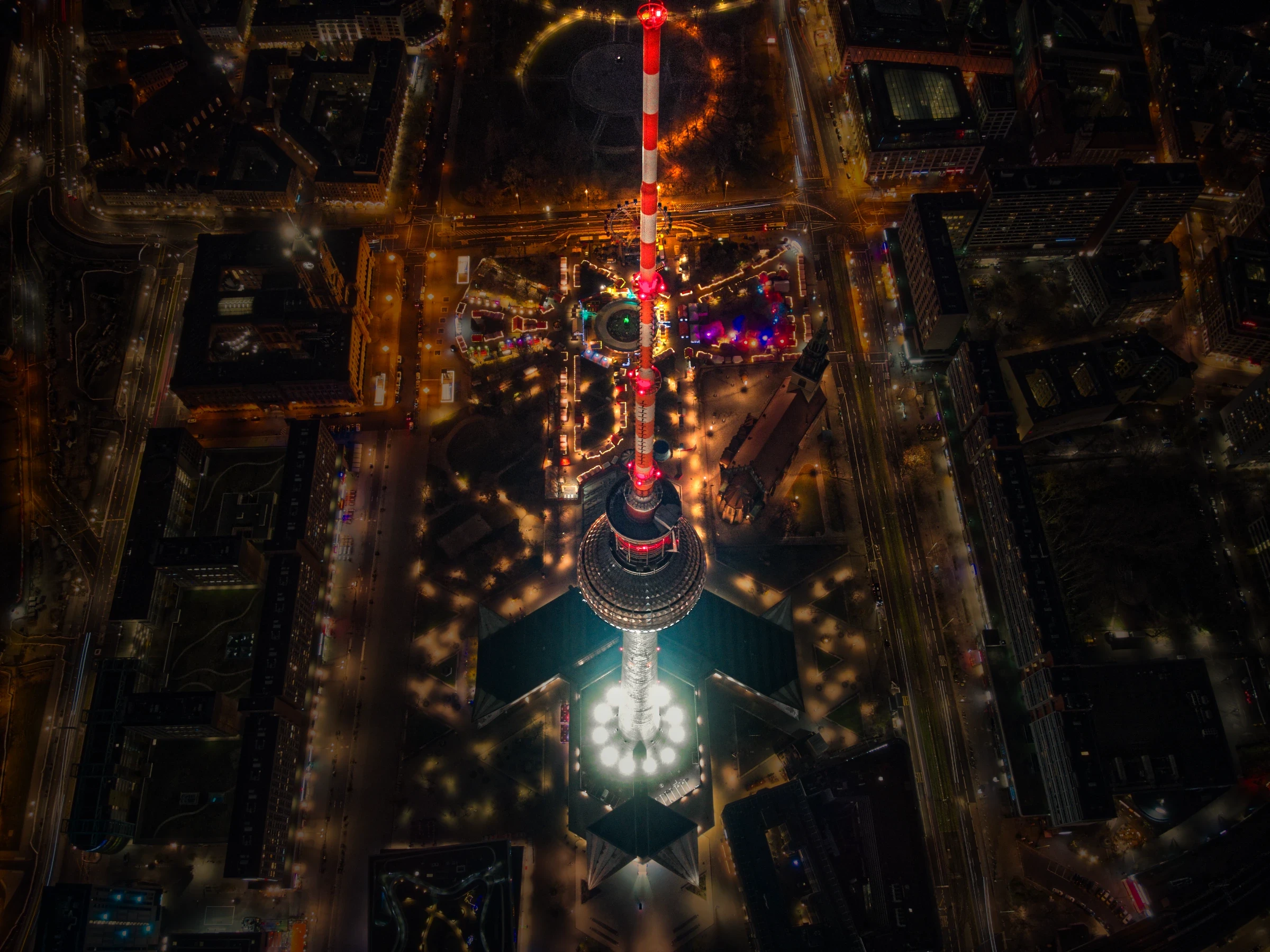 Senkrechte Drohnenaufnahme des Berliner Fernsehturms von oben. Der beleuchtete Turm steht im Zentrum der Berliner Innenstadt und des Weihnachtsmarktes am Alexanderplatz.