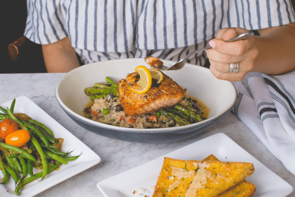 a woman holding a fork to eat roasted salmon with asparagus