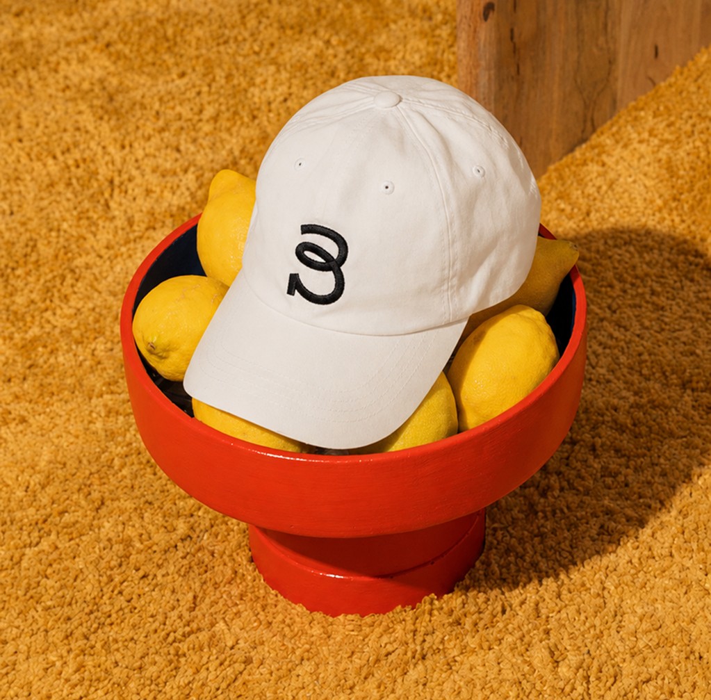 White branded cap with turquoise logo placed on fresh lemons in a red bowl