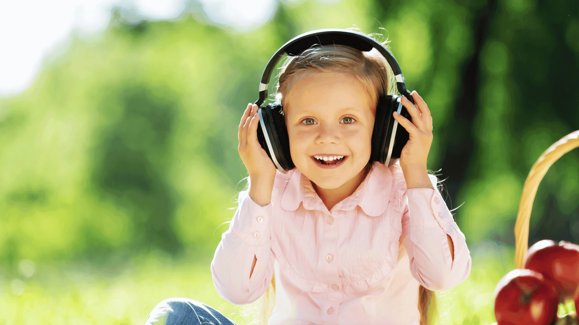 A child sitting outside in the sunshine, wearing headphones, smiling, and looking happy while listening to HushAway®’s Sound Sanctuary.