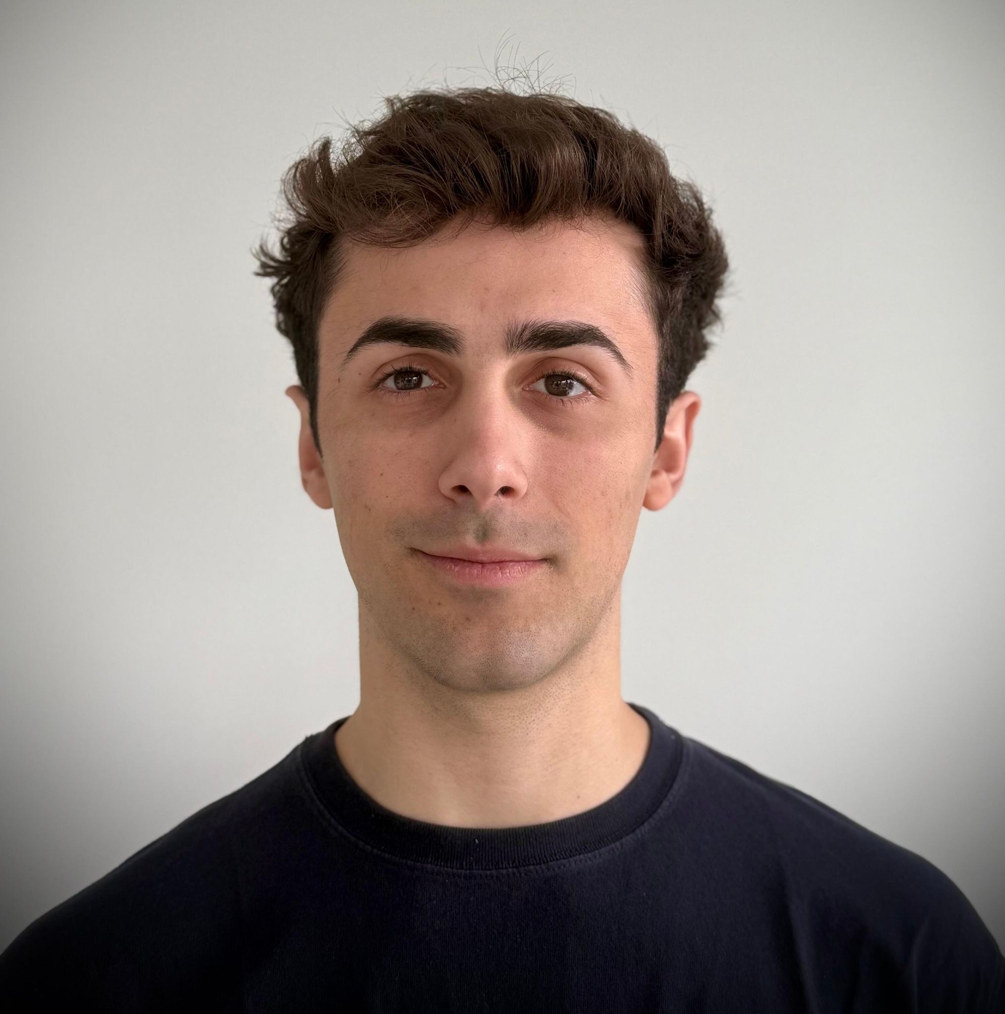 Portrait of a man with dark hair wearing a black shirt against a plain light background.