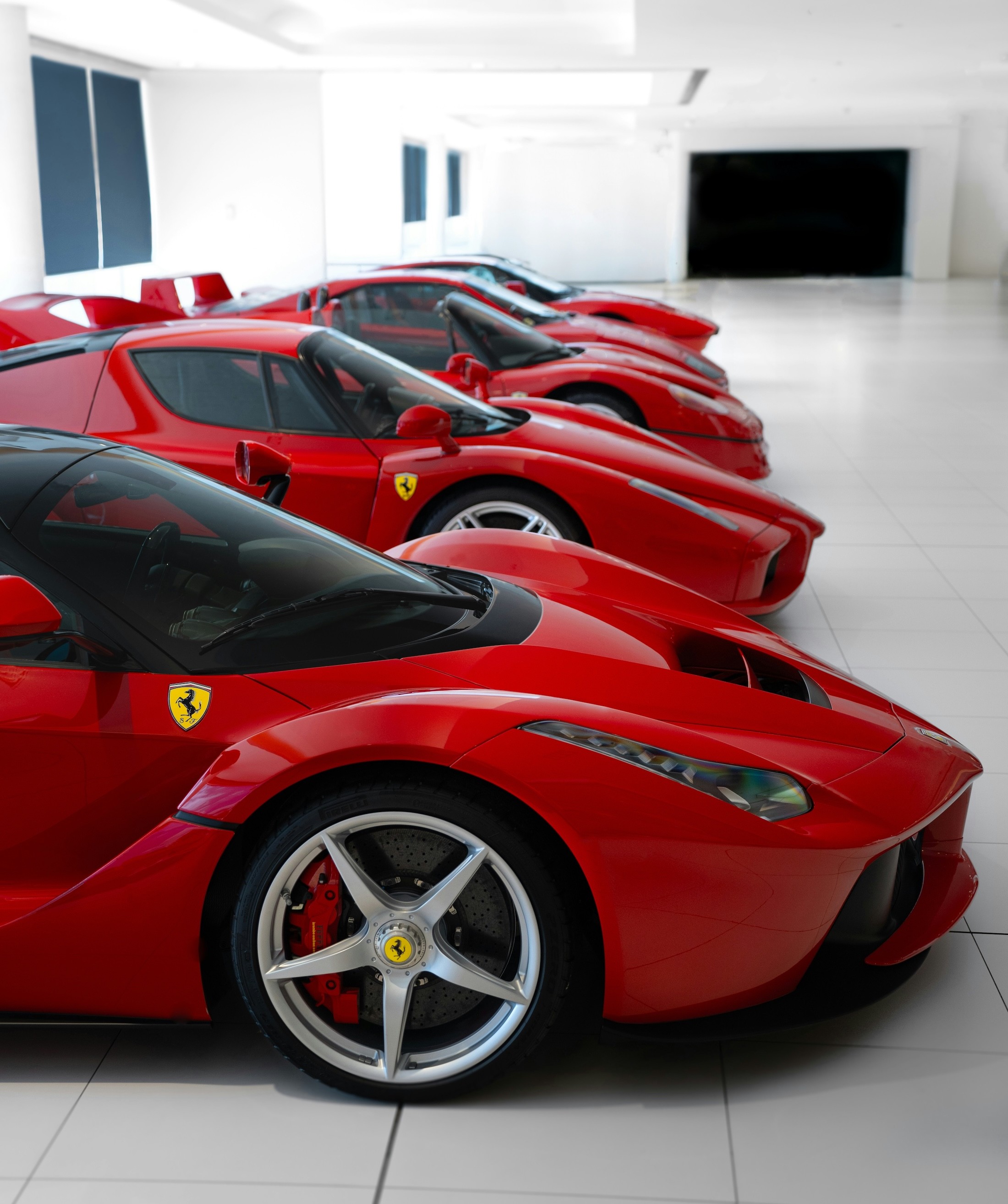 A sleek row of vibrant red Ferrari sports cars is showcased in a pristine, spacious showroom with a glossy tiled floor, highlighting the brand's luxurious and high-performance appeal.