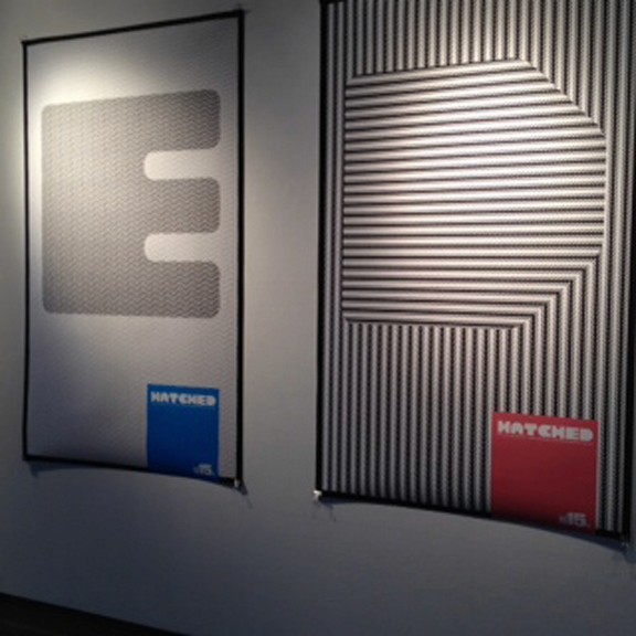 A set of black and white printed posters that show a letter and a colorful square near a corner with text Hatched.