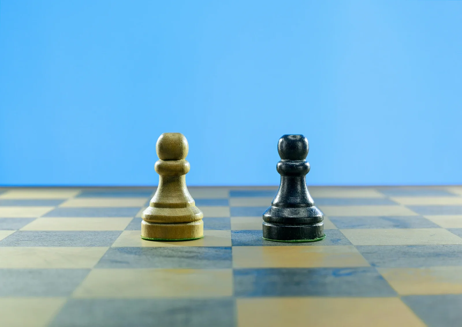 White and black chess pawns facing each other on a blue and beige checkered board against a blue background.