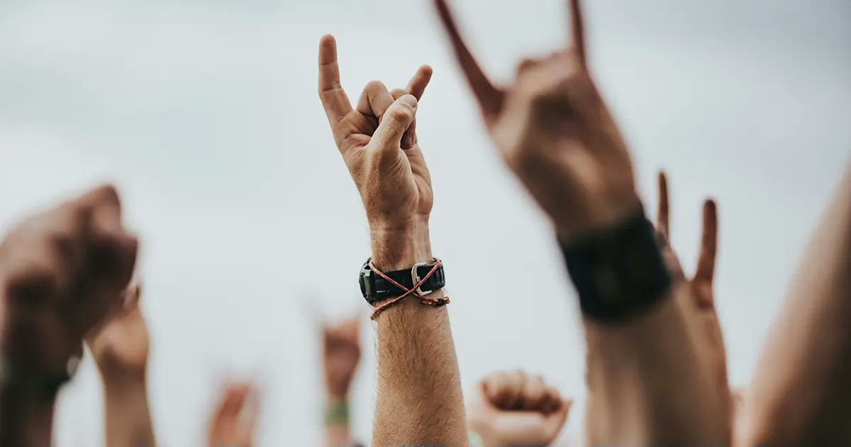 Crowd raising hands with rock and metal horns at an outdoor music festival.