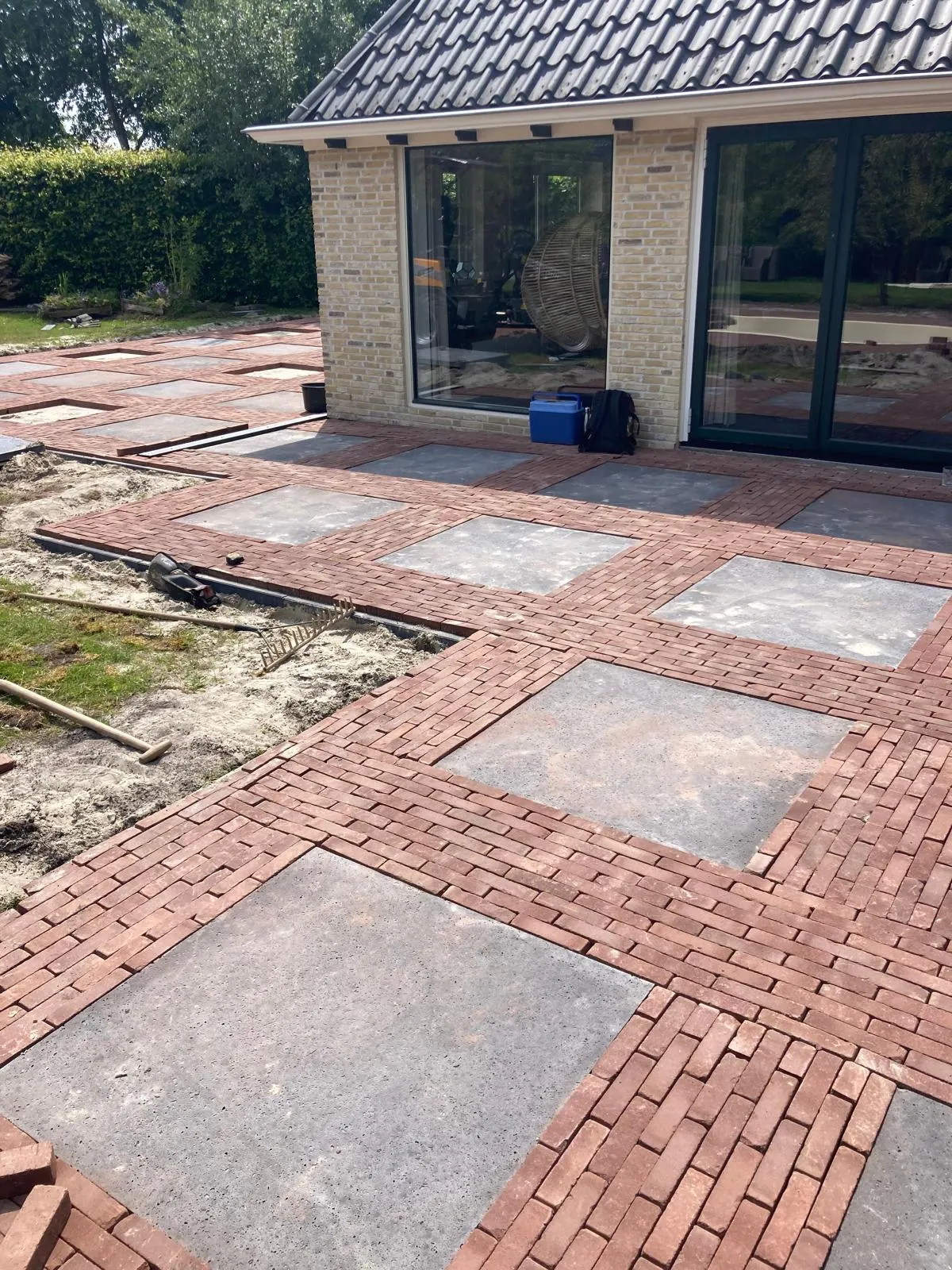 Strakke terrasbestrating met grote tegels en gebakken klinkers bij moderne woning in Jubbega