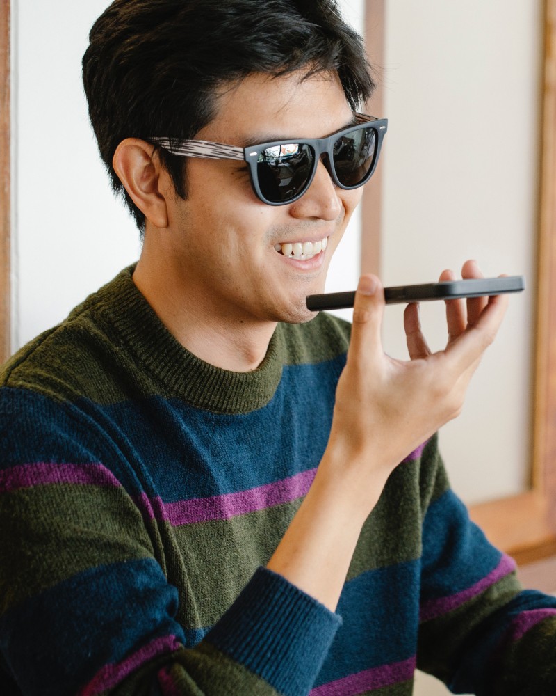 A man in dark-tinted glasses holding a phone and smiling