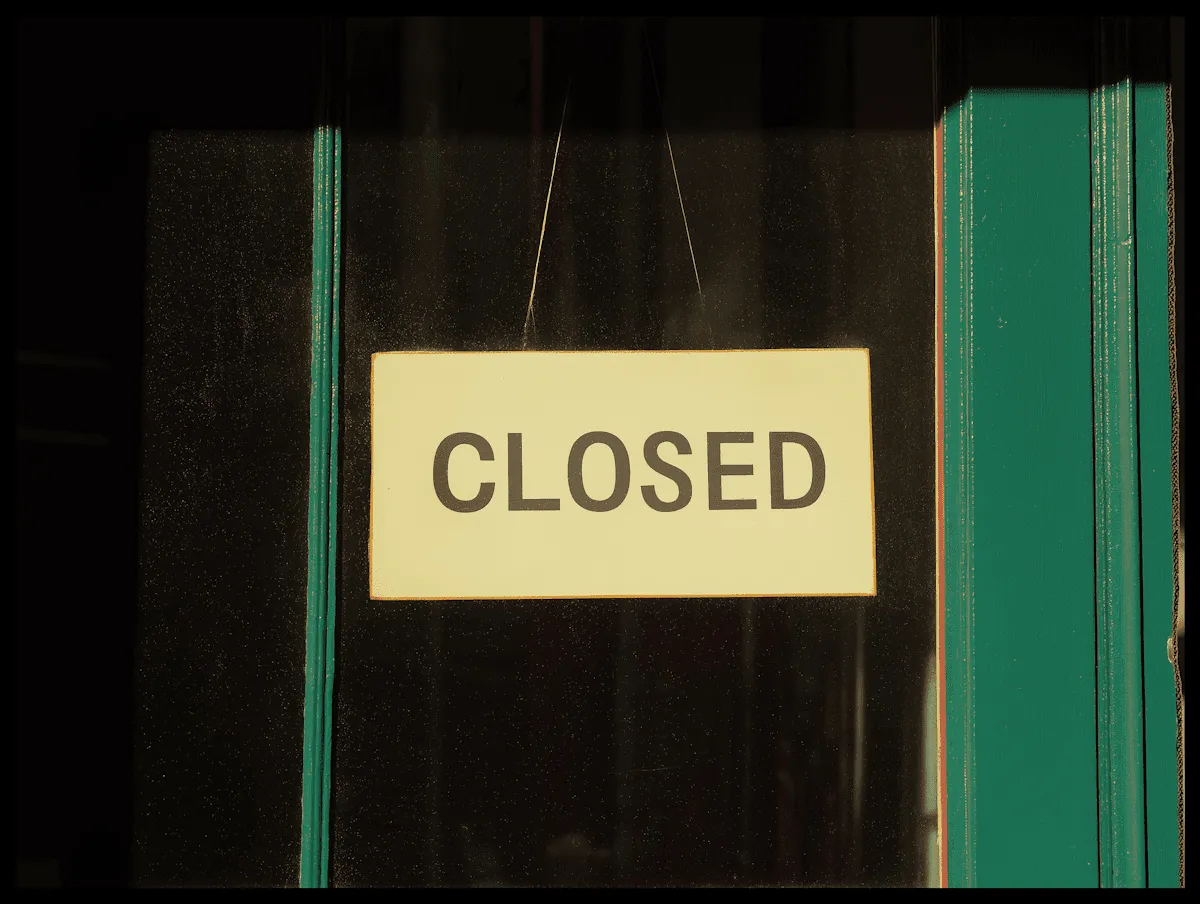 A sign that reads "CLOSED" attached to a door or window with a dark background and green trim.