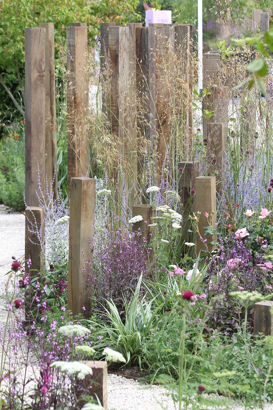 A garden scene featuring tall wooden posts, surrounded by greenery and plants, creating a serene atmosphere.