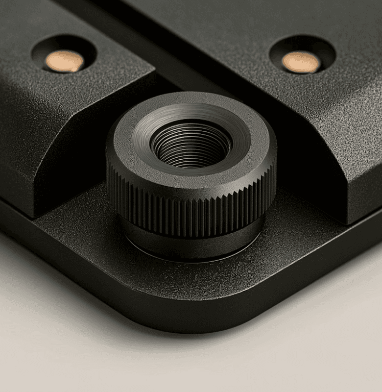 Close-up of a black metal threaded knob on a textured mechanical surface.
